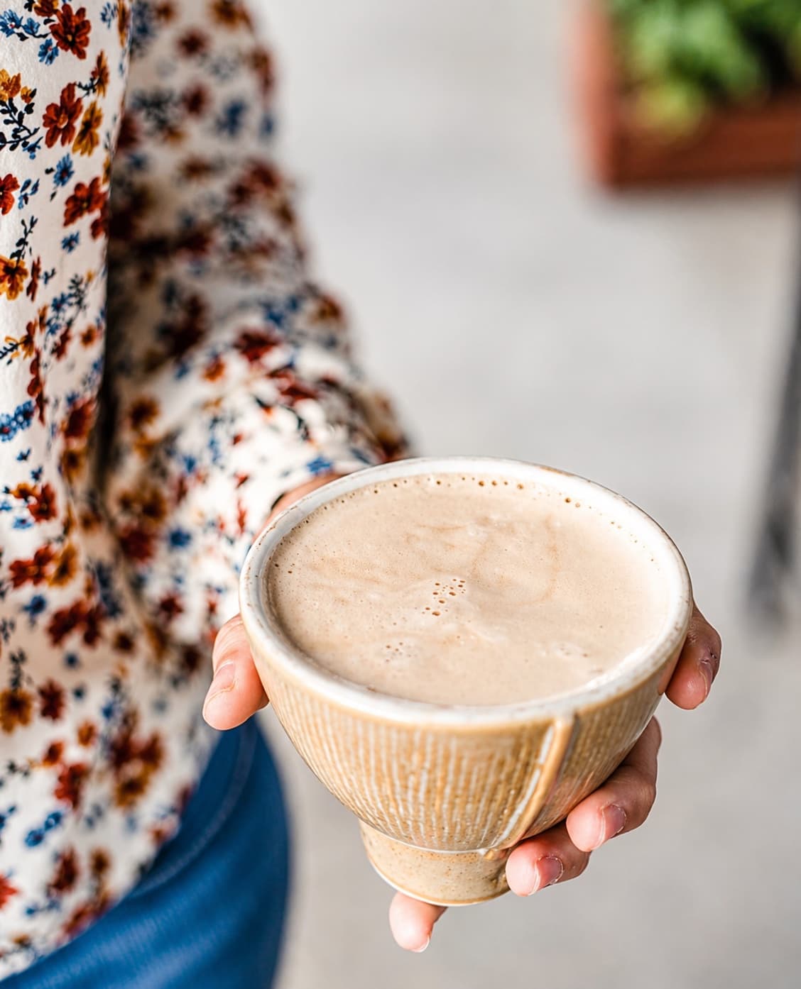 A stoneware bowl held in two hands, foam settling on a hot drink.