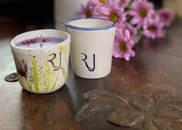 Ceramic candle holder and cup featuring blue script and hand-painted details on a dark wood surface.