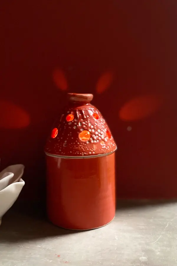 Red ceramic candle holder with a perforated domed lid, casting warm light against a red backdrop.