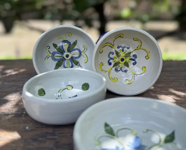 Four small white ceramic bowls with hand-painted blue and yellow floral patterns on a wooden table.