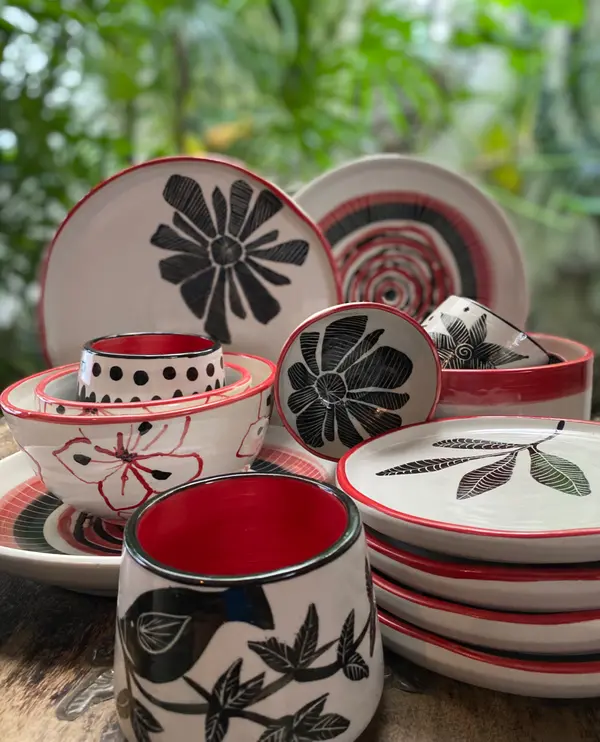 Collection of white ceramic plates, bowls, and mugs with black hand-painted nature motifs and red accents.