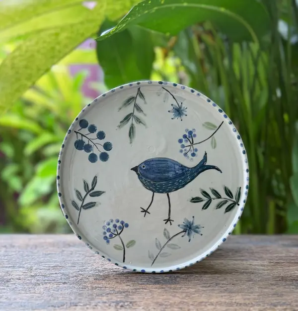 White ceramic plate with hand-painted blue bird, berries, and green leaves on a wooden table.