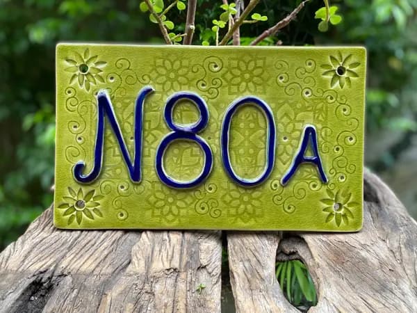 Green crackle glaze house number plaque with blue embossed N80A text and floral patterns on weathered wood.