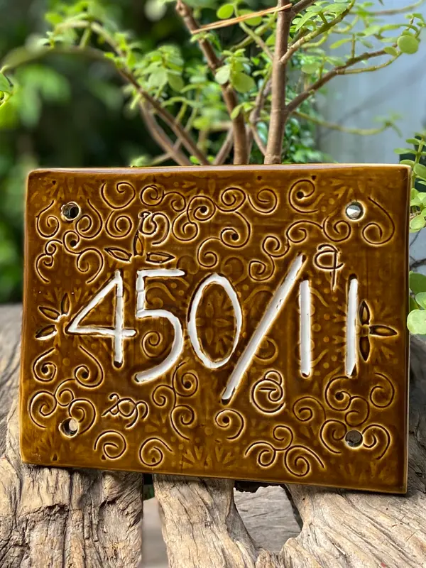 Handcrafted brown ceramic house number plaque with white numbers 450/11 and intricate swirl patterns.
