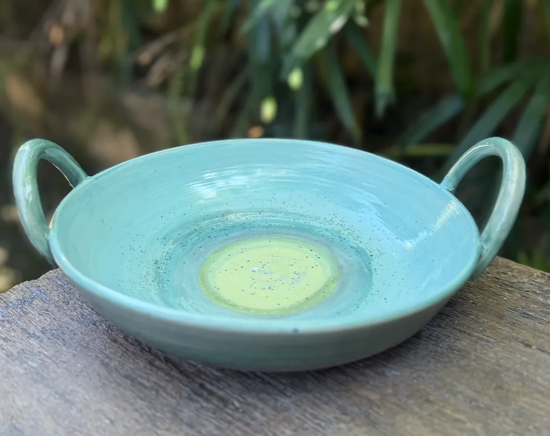 Turquoise ceramic bowl with two handles and a pale green center, resting on a wooden surface.