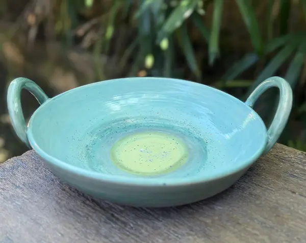 Turquoise ceramic bowl with two handles and a pale green center, resting on a wooden surface.