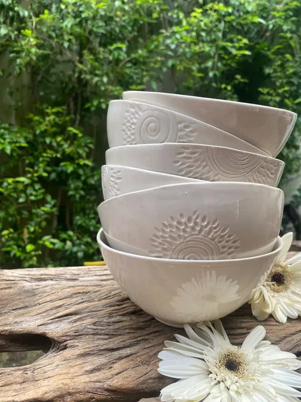 Stacked white ceramic bowls with embossed floral patterns on a rustic wood surface against a green garden background.