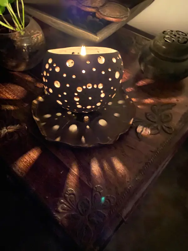 Black ceramic candle holder with circular cutouts casting warm light onto a dark wooden surface.
