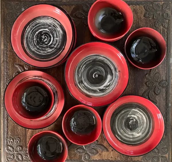 Red ceramic dinnerware set with black and white spiral designs arranged on a carved wooden surface.