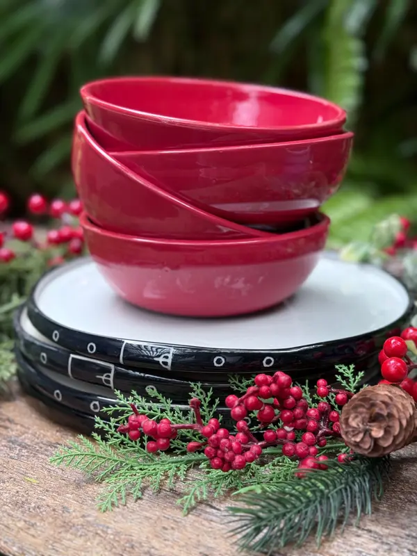 Stack of three red ceramic bowls on three black and white plates with Christmas greenery and berries.