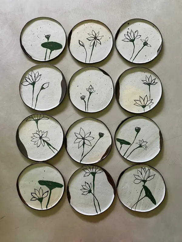 Twelve white ceramic plates with dark green lotus flower illustrations arranged in a 3x4 grid.