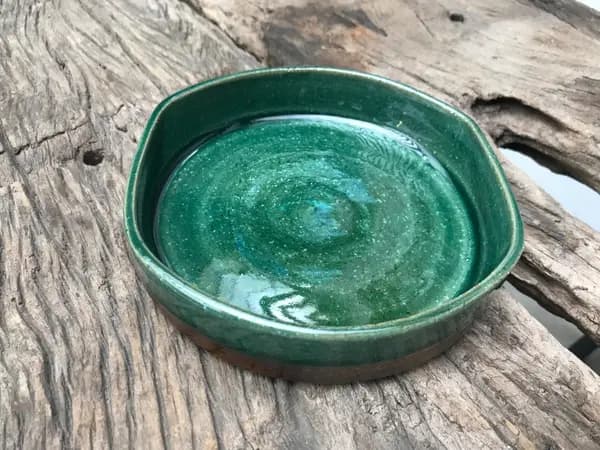 Small square dark green ceramic trinket plate with swirling glaze on a weathered wooden background.