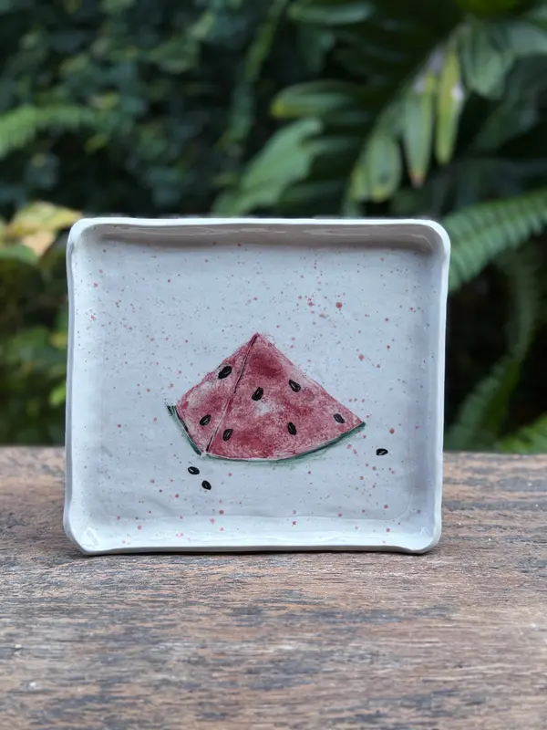 Square ceramic trinket plate with a hand-painted watermelon slice and pink speckles on a white glaze.