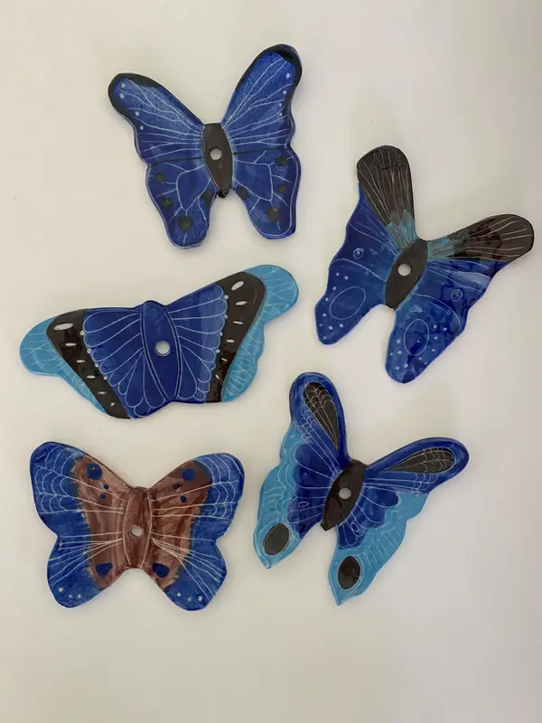 Five hand-painted blue ceramic butterflies with detailed wing patterns and central holes on a white background.