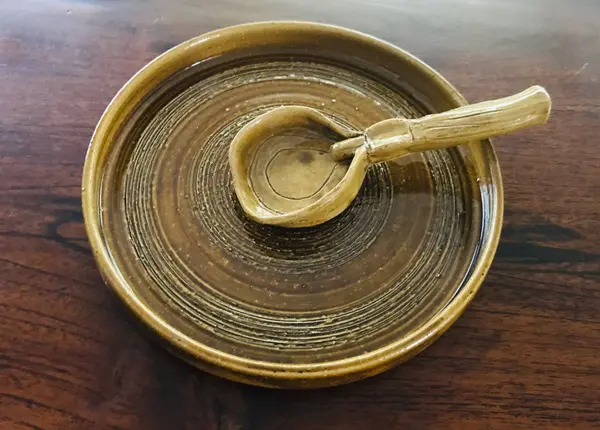 Brown glazed ceramic spoon rest featuring a textured plate and a matching handmade spoon on a dark wood table.