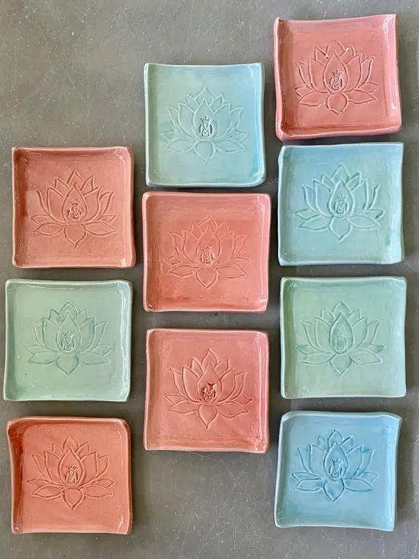 Ten square ceramic trinket plates in pink and light blue with an embossed lotus flower design.