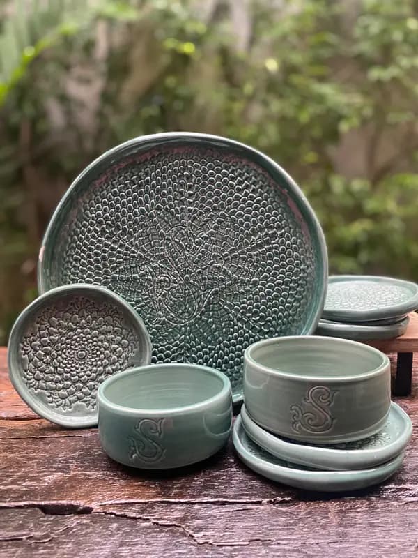 Sage green ceramic set with a large textured mandala platter, monogrammed bowls, and matching coasters on a wood surface.