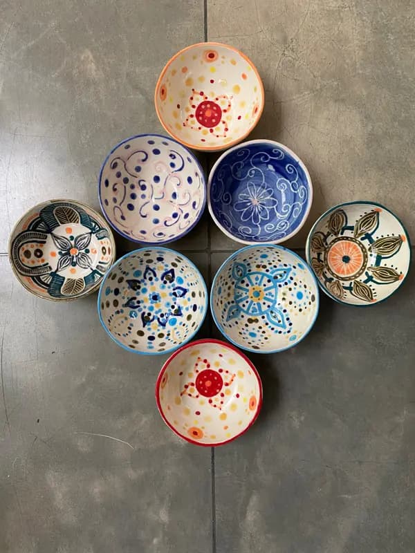 Seven hand-painted ceramic dip bowls with various colorful patterns arranged on a grey stone surface.