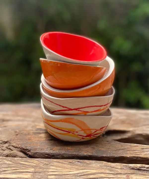 Stack of five ceramic bowls with red and orange glazes and painted abstract lines on a rustic wood surface.