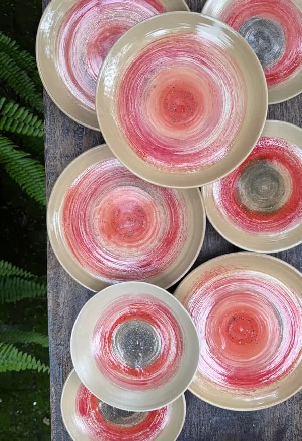 Top-down view of beige ceramic plates with vibrant red and pink spiral glaze patterns on a wooden surface.