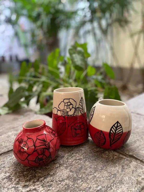 Three ceramic vases with red and white glaze and black line art drawings of flowers and leaves on a stone surface.