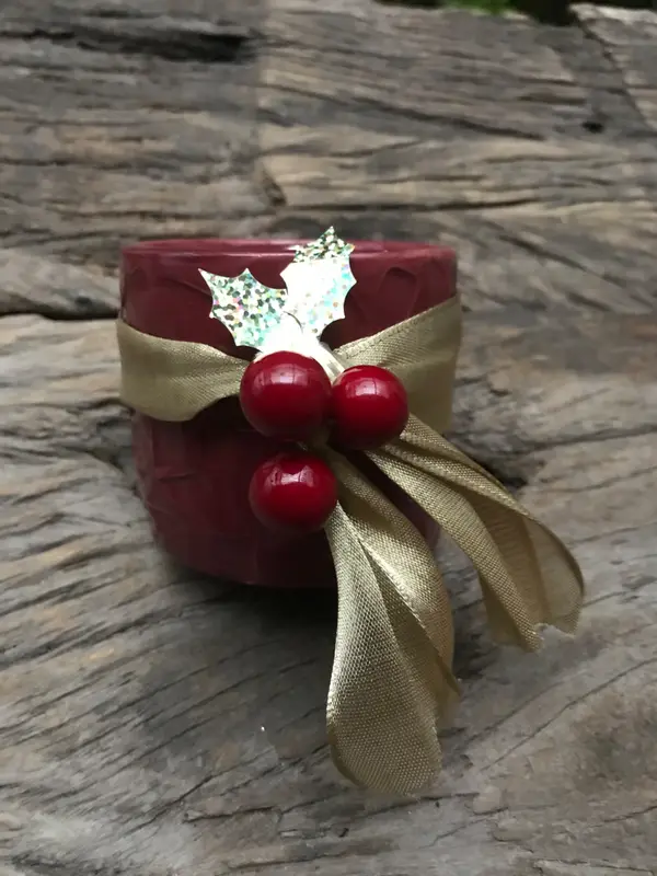 Red textured ceramic pot decorated with gold ribbon and red berries on a rustic wood background.