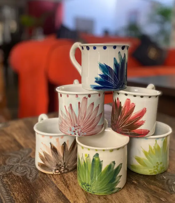 Six stacked ceramic mugs with hand-painted colorful flower designs and dotted rims on a wooden table.