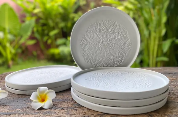 White ceramic plates with embossed lace patterns on a wooden table with a frangipani flower.