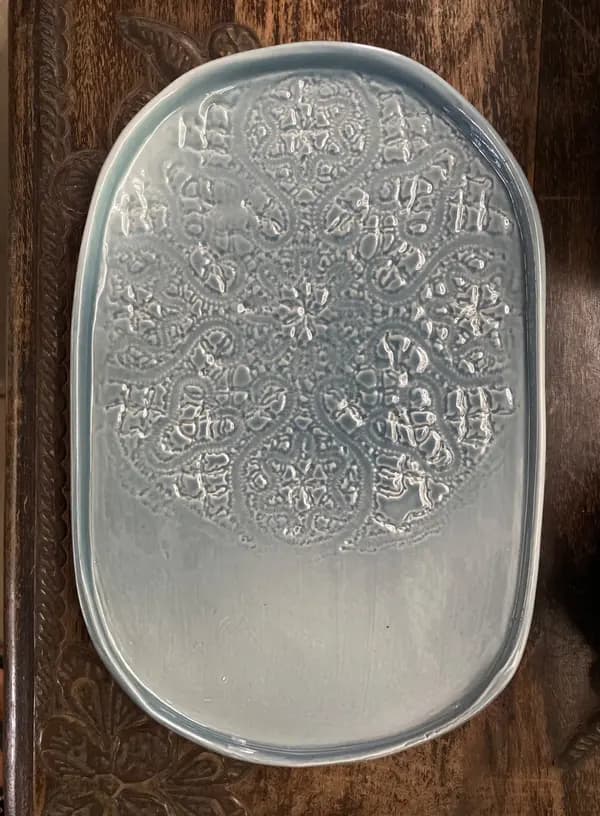 Light blue oval ceramic platter with a glossy glaze and an intricate embossed lace mandala design on one side.