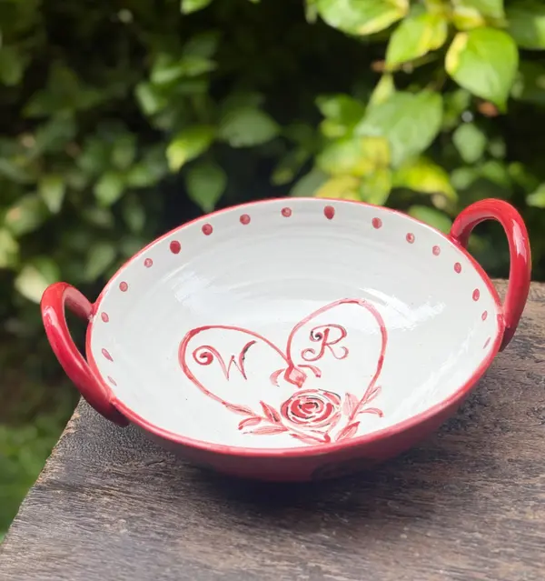 White ceramic bowl with red handles featuring a hand-painted heart with initials and a rose design.