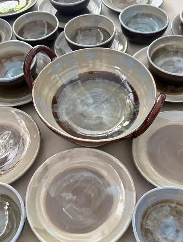 A collection of handmade beige and brown ceramic pottery, including a large handled bowl and several plates.