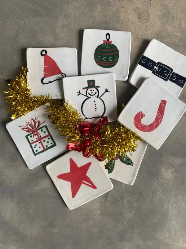 Set of square white ceramic coasters with hand-painted Christmas designs including a snowman and candy cane.