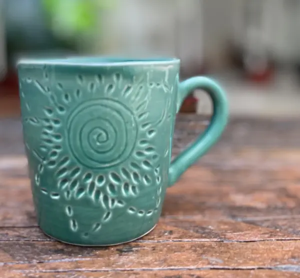 Turquoise ceramic mug with a hand-carved spiral sunburst pattern on a rustic wooden table.