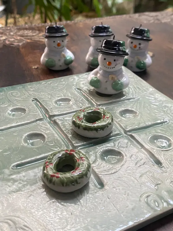 Ceramic tic-tac-toe board with snowman and wreath pieces in glossy light green and white glaze.