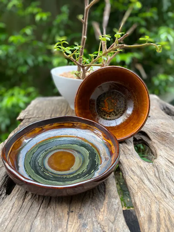 Two handmade ceramic bowls with amber, dark green, and black glazes on a weathered wood surface.