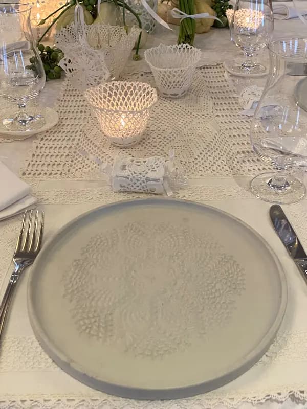 White ceramic plate with a central lace imprint on an elegant tablescape with white lace candle holders.