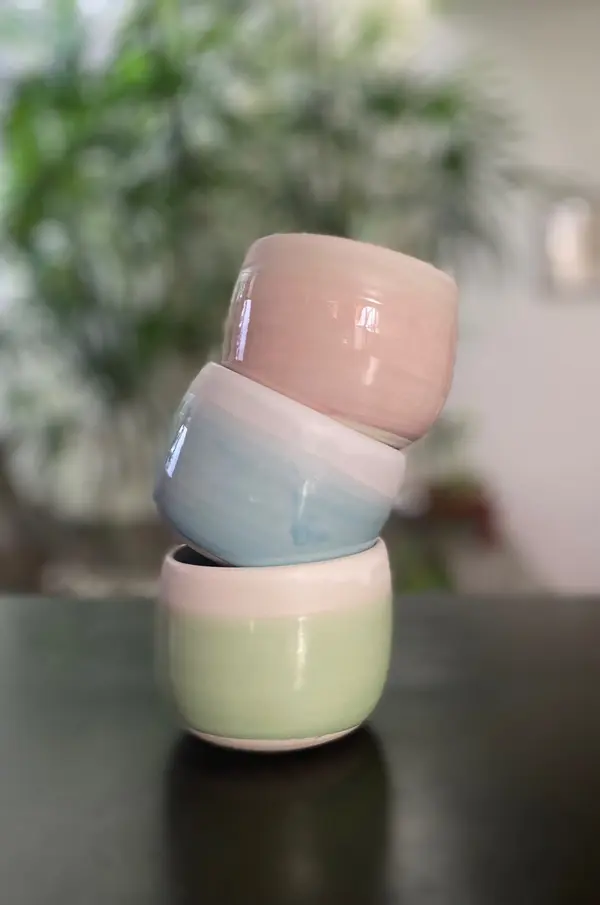 Three stacked handmade ceramic bowls in pastel pink, light blue, and light green with a glossy finish.