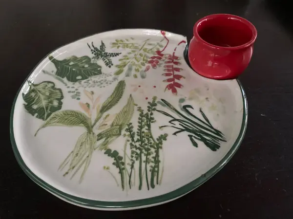White ceramic plate with green leaf motifs and a small integrated red dip bowl.