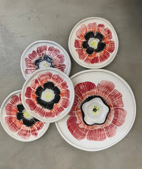 Five white ceramic plates and a small bowl with hand-painted red poppy designs and black centers.