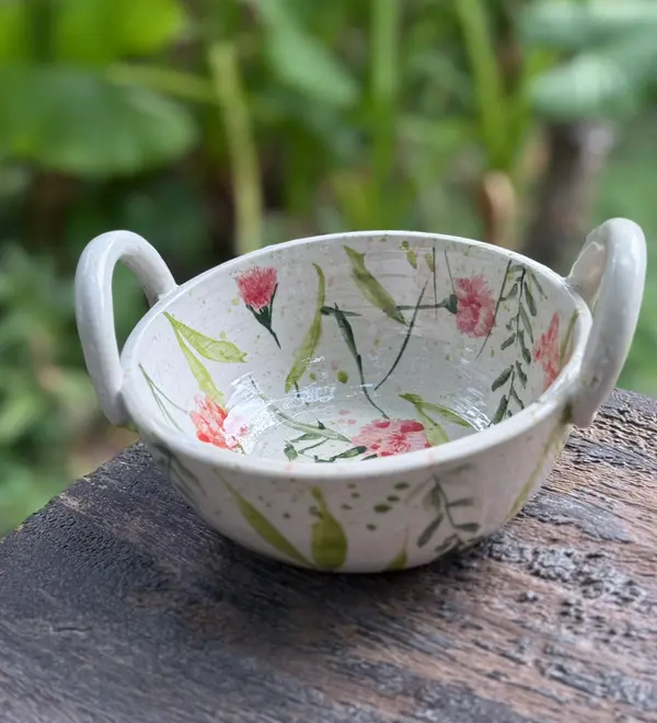 White ceramic handled bowl with hand-painted pink flowers and green leaves, sitting on a wooden surface.