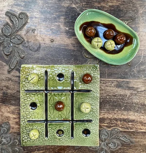 Ceramic tic-tac-toe board with light green textured glaze and rounded playing pieces on a wooden surface.