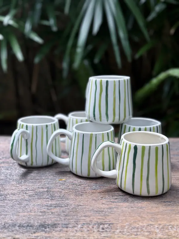 A group of white ceramic mugs with hand-painted vertical green stripes on a rustic wood surface.