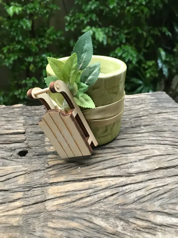 Small light green textured ceramic pot decorated with a wooden sled and faux green leaves on a rustic wood surface.