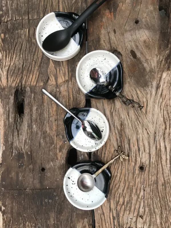 Four black and white speckled ceramic spoon rests with assorted spoons on a rustic wooden surface.
