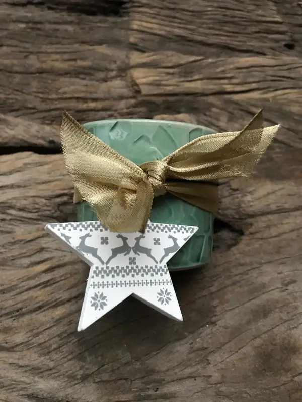 Small sage green textured ceramic cup with a gold ribbon and a star-shaped reindeer ornament on wood.