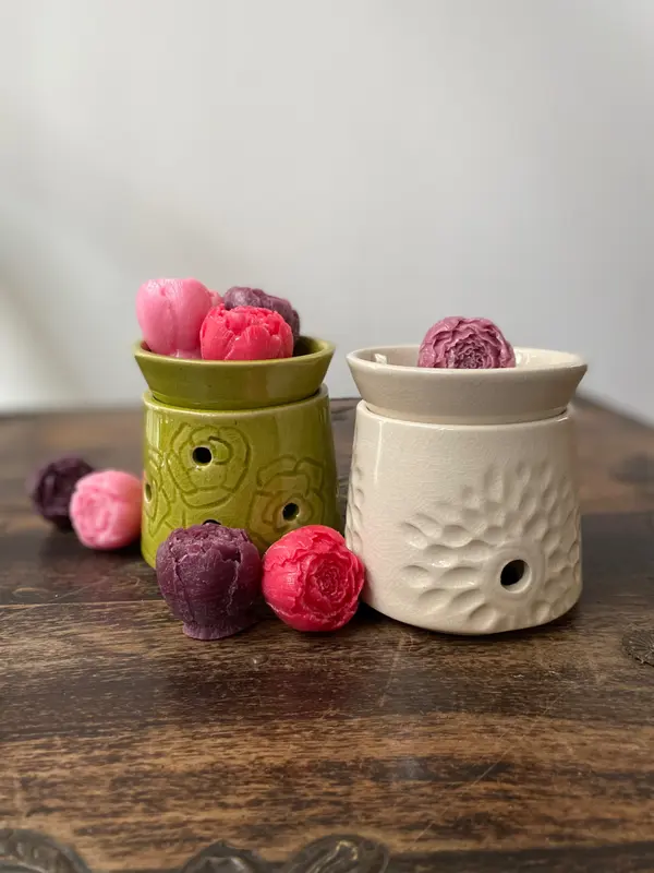 Two ceramic oil burners, one apple green and one white, with flower-shaped wax melts on a wooden table.