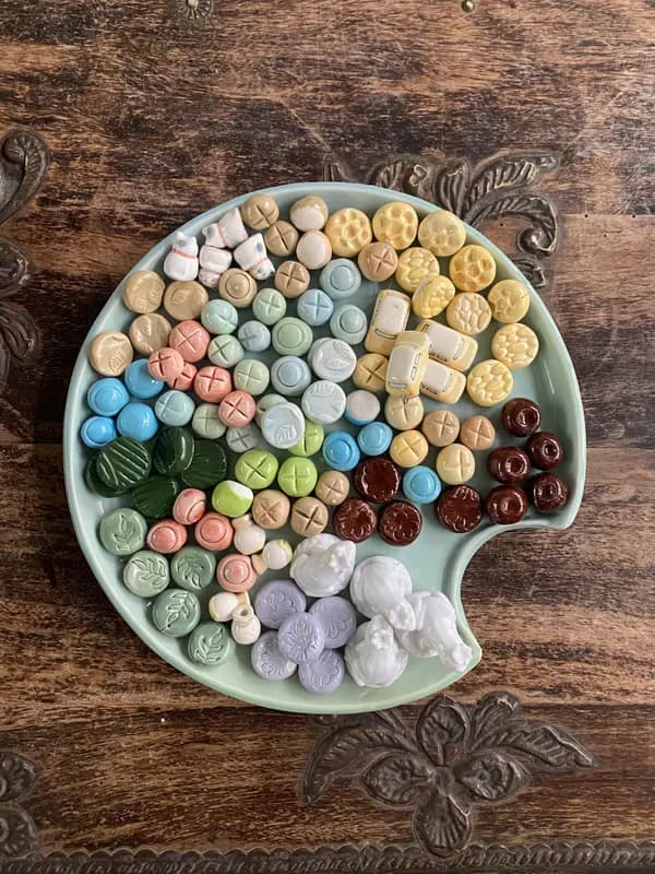 Colorful ceramic buttons, cats, and cars arranged on a mint green palette-shaped platter on a wooden surface.