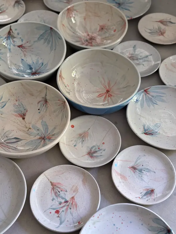 Collection of white ceramic bowls and plates decorated with delicate hand-painted blue and pink flowers.