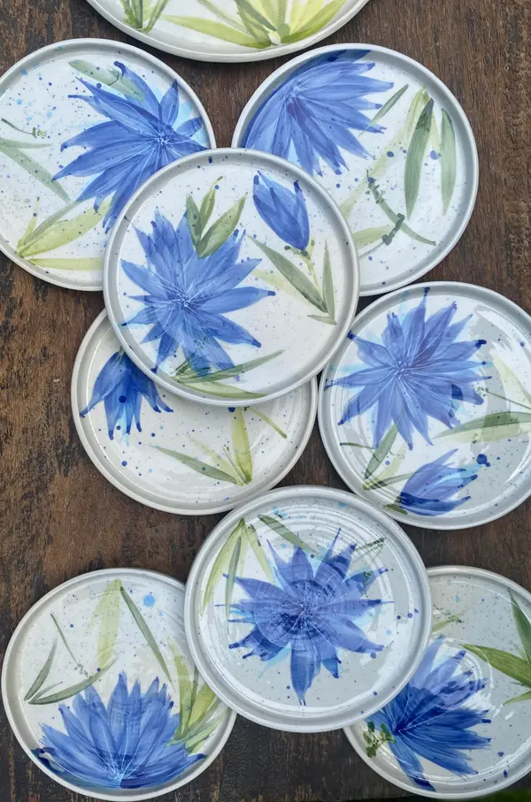 Hand-painted white ceramic plates with blue floral patterns and green leaves on a wooden background.