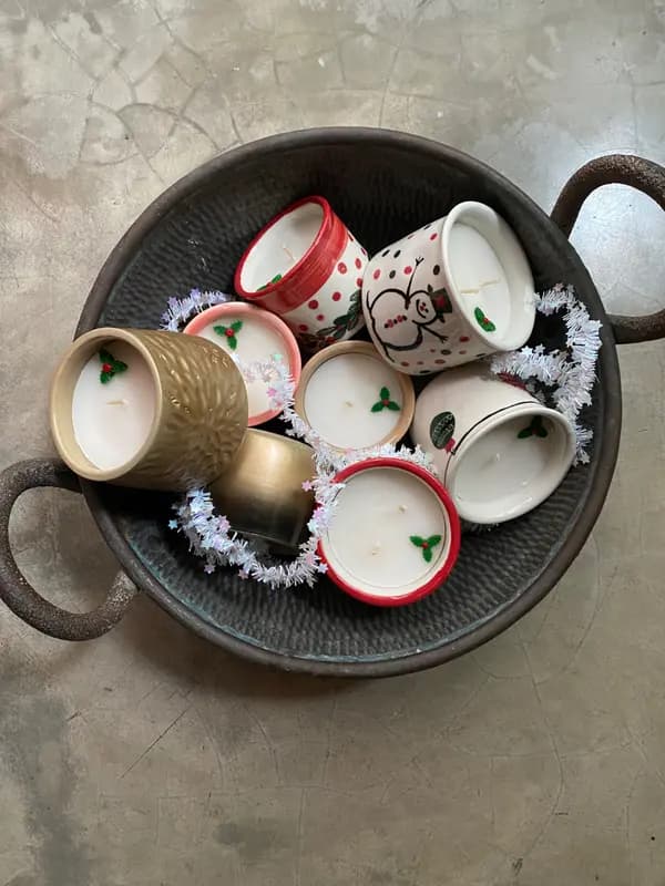 Festive hand-painted ceramic candle pots with snowman and holly designs in a metal basin with silver tinsel.